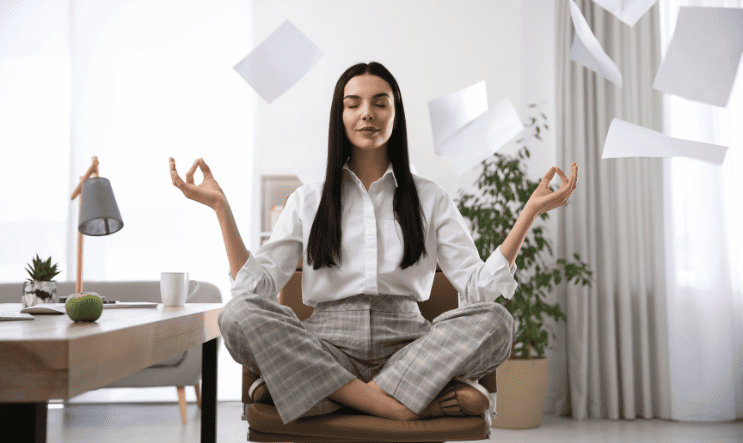 Calm woman meditating at her desk in a modern office with papers flying around – Stress Relief Therapy for anxiety and burnout at Integrated Wellness Services in Plainview